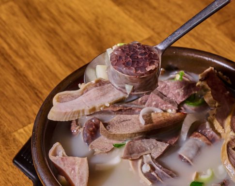 숟가락으로 순대를 떠 올린 국밥 뚝배기 — 국물 속 내장·고기 건더기