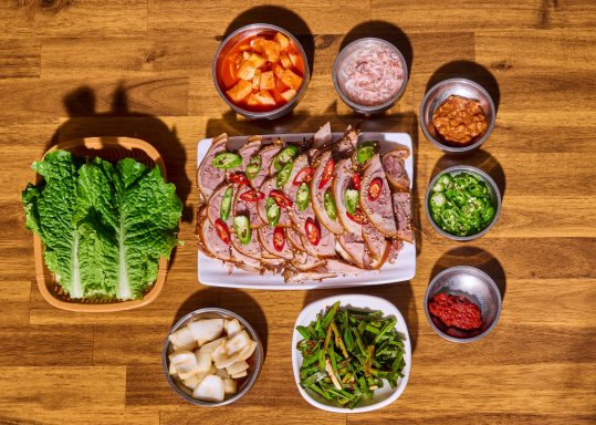 위에서 본 상 — 네모난 흰 접시에 썬 족발(홍고추·청양고추 올림), 둘레에 알배추 쌈, 깍두기, 새우젓, 쌈장, 썬 청양고추, 양념장, 양파절임(무), 부추무침