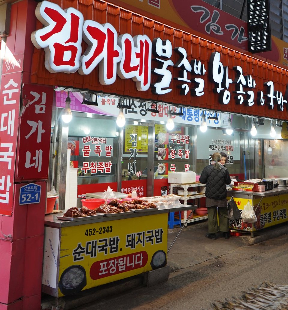 새마을중앙시장 통로의 가게 앞 — 빨간 글씨 간판과 판대 위 족발 쟁반