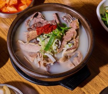 검은 뚝배기에 담긴 뽀얀 국물의 돼지국밥 — 돼지고기와 내장, 붉은 다대기, 파